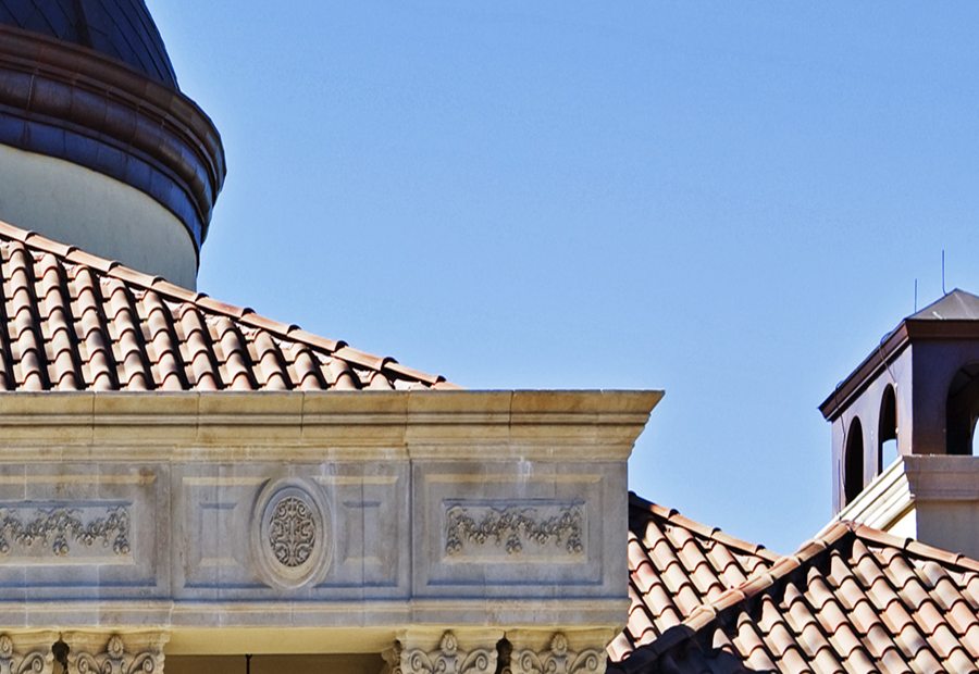 Clay tile roof field meeting a carved stone cornice, with a bell tower behind